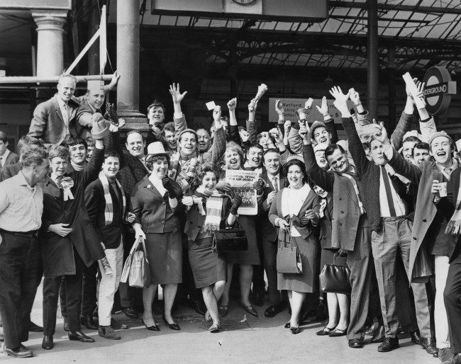 Liverpool fans at Euston Station, London, 1st May 1965.  They are on their way to see their team play Leeds United in the FA Cup final at Wembley. A woman (centre) is holding a copy of the Evening Standard newspaper with the headline 'Liverpool trying for cup double'. Liverpool later won the final 2-1. (Photo by Central Press/Hulton Archive/Getty Images)